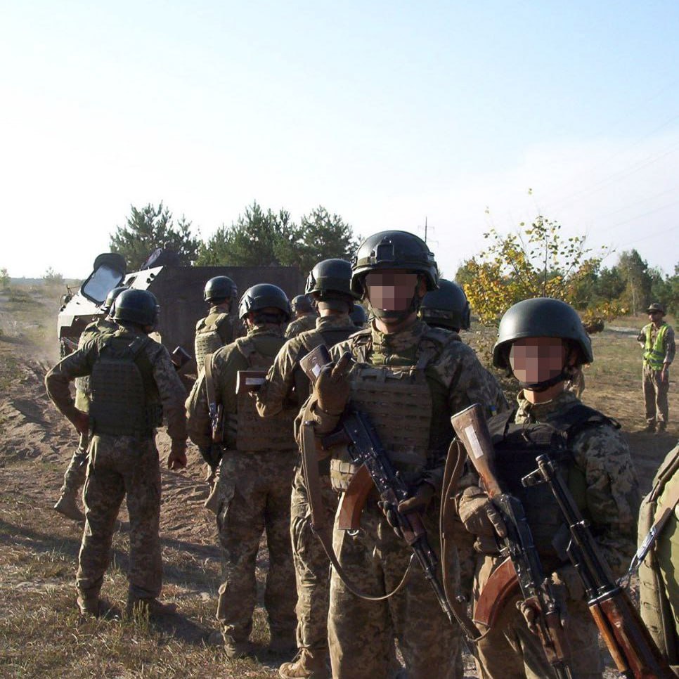 Group of soldiers in military uniforms and helmets standing outdoors during training or deployment.