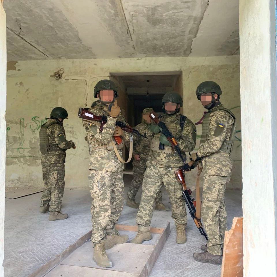 Soldiers in military gear standing inside an abandoned building during a training exercise or operation.