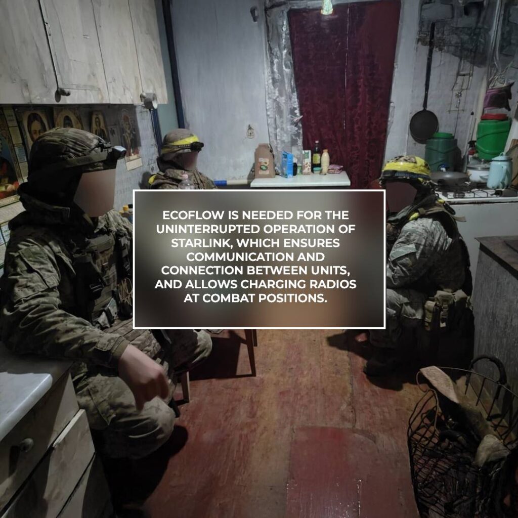 Soldiers in tactical gear sit in a modest kitchen while discussing plans, with equipment and supplies visible on the table and surroundings.