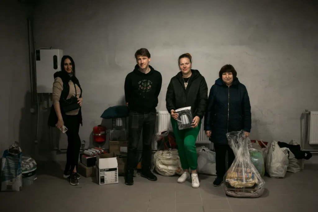 A group of people standing inside a room with supplies, including bags and boxes, ready for distribution during a humanitarian mission.