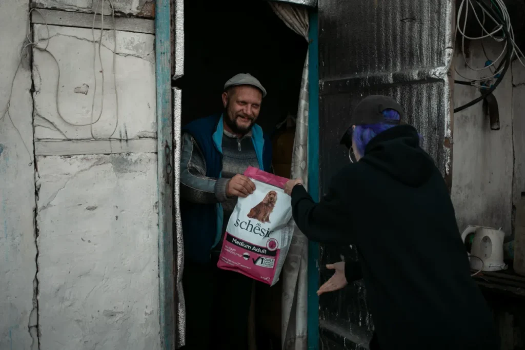 A volunteer handing a bag of dog food to a man standing at the door of his home, with a warm and friendly interaction captured.